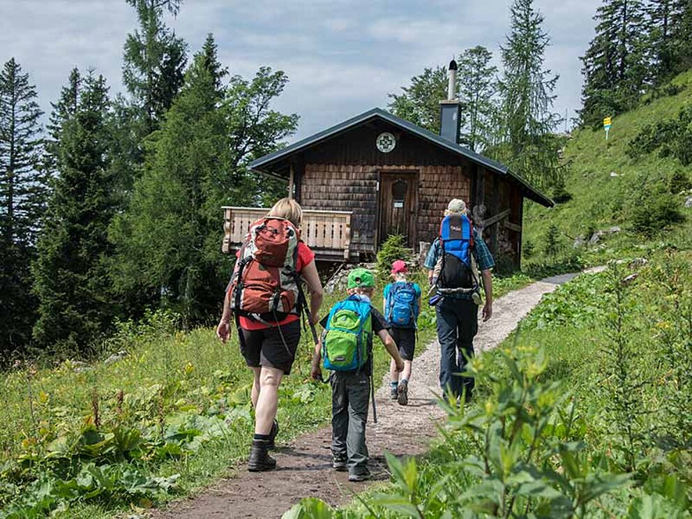 4 Wanderer von hinten am Weg zu einer kleinen Almhütte