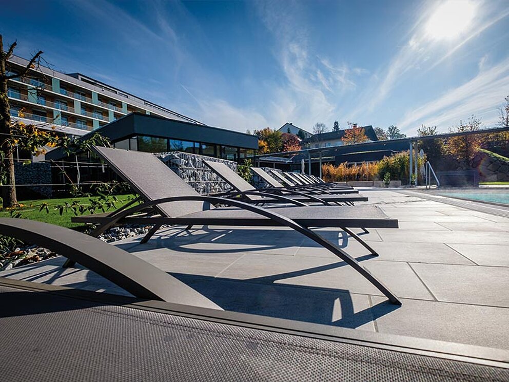 Außenbereich mit Relax-Liegen, Außenpool und dem Hotel im Hintergrund.