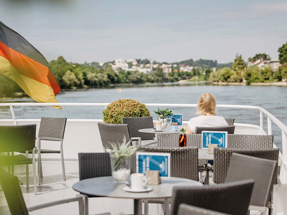 Eine Frau sitzt am Obereck an einem Tisch und blickt auf die Donau