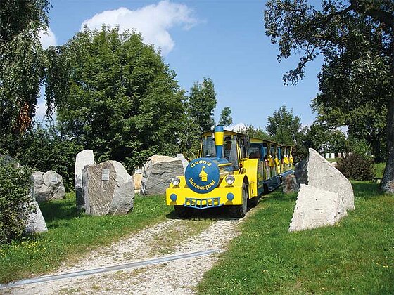 Der gelbe Bummelzug der Erlebniswelt fährt an den Granit-Exponaten vorbei.