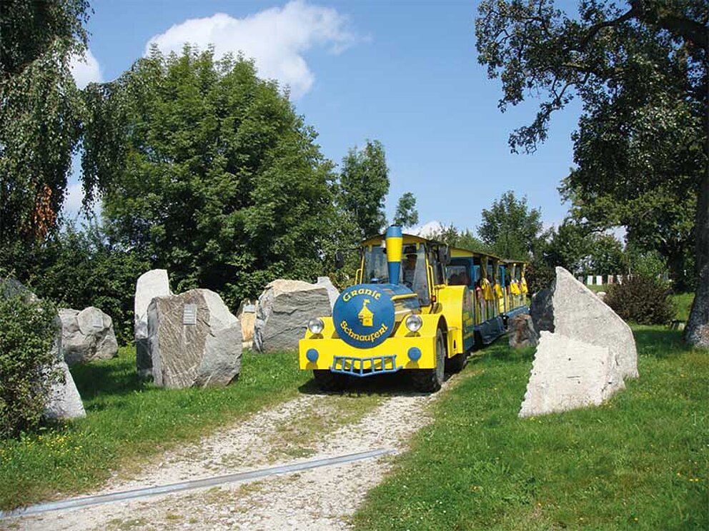 Der gelbe Bummelzug der Erlebniswelt fährt an den Granit-Exponaten vorbei.