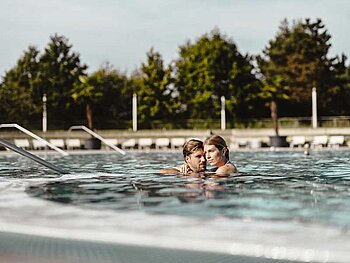Mann und Frau umarmen sich im Outdoorbecken des Spa Resort Geinberg
