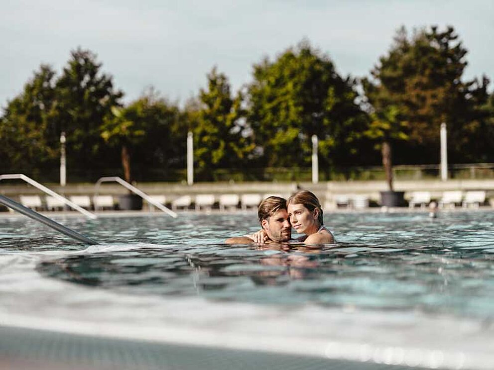 Mann und Frau umarmen sich im Outdoorbecken des Spa Resort Geinberg