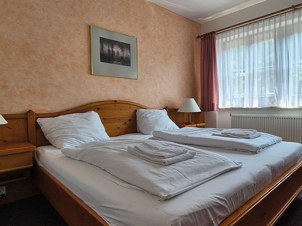 Zimmer mit Doppelbett, Nachtkästchen und Teppichboden