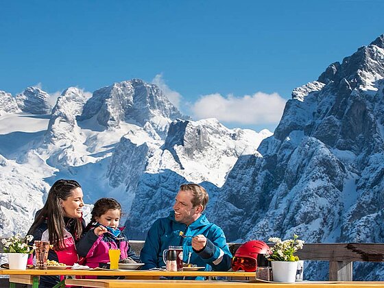 Eine Familie beim Mittagessen, im Hintergrund der Dachstein
