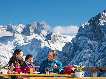 Eine Familie beim Mittagessen, im Hintergrund der Dachstein