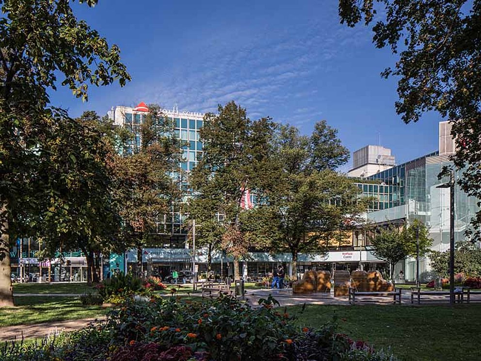 Blick von Volksgarten durch die Bäume auf Hotel Schillerpark in Linz