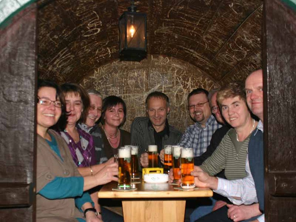 Besucher in geselliger Runde sitzen in einem riesigen Bierfass um einen Tisch und stoßen gemeinsam an.