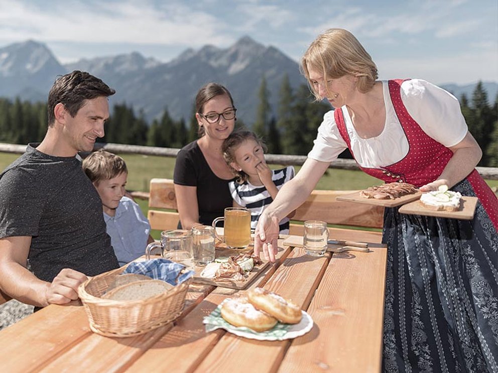 Die Wirtin serviert einer Familie Köstliches aus der Region