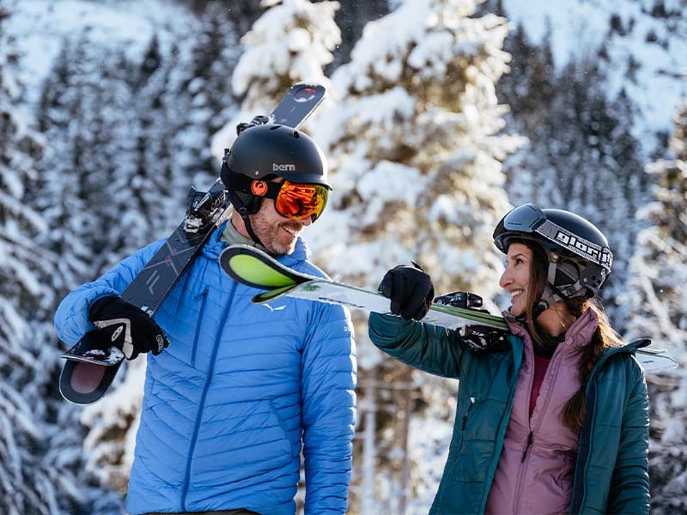 ein Paar mit ihren Skiern auf den Schultern