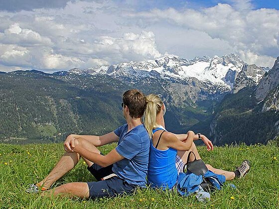 Paar sitzt in der Wiese auf der Zwieselalm in Gosau und blickt auf die umliegende Bergwelt