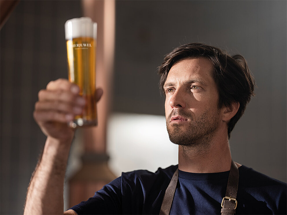 Der Braumeister hält ein kleines Bier mit Schaumkronen in der Hand und überzeugt sich von der Qualität.