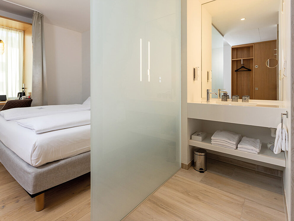 Zimmer mit einer Glasscheibe abgetrennten Badezimmernische.