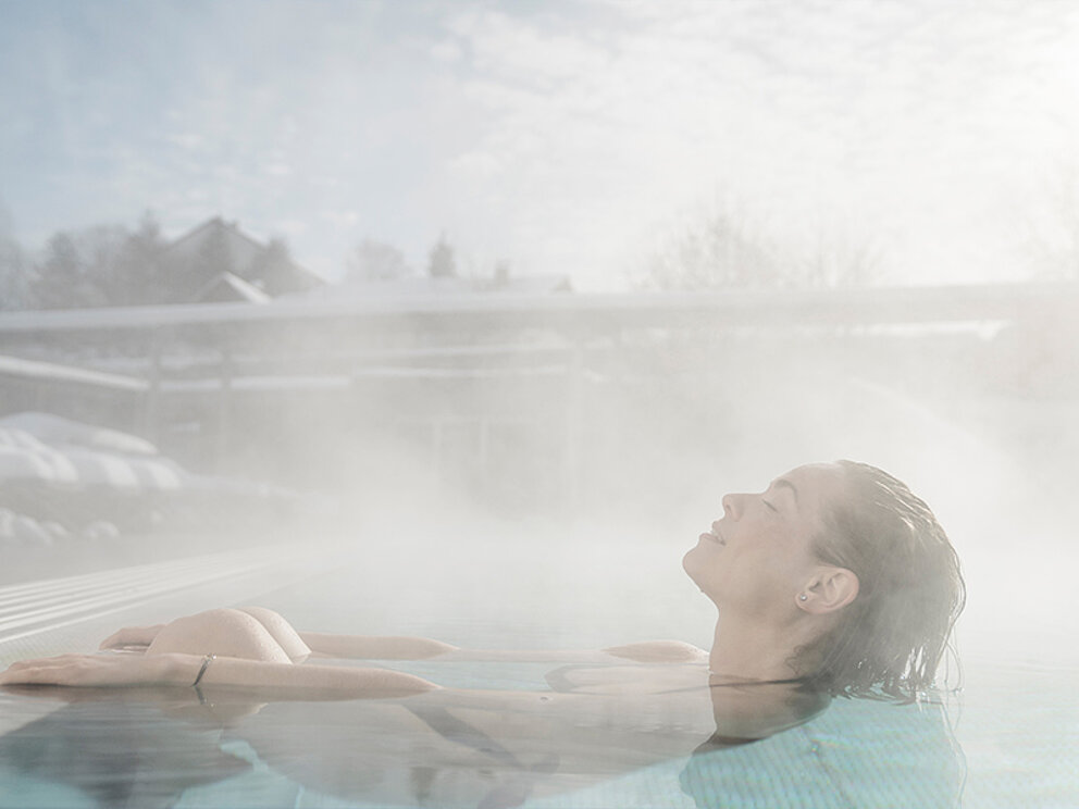 Dame entspannt im Außenpool in winterlicher Landschaft.