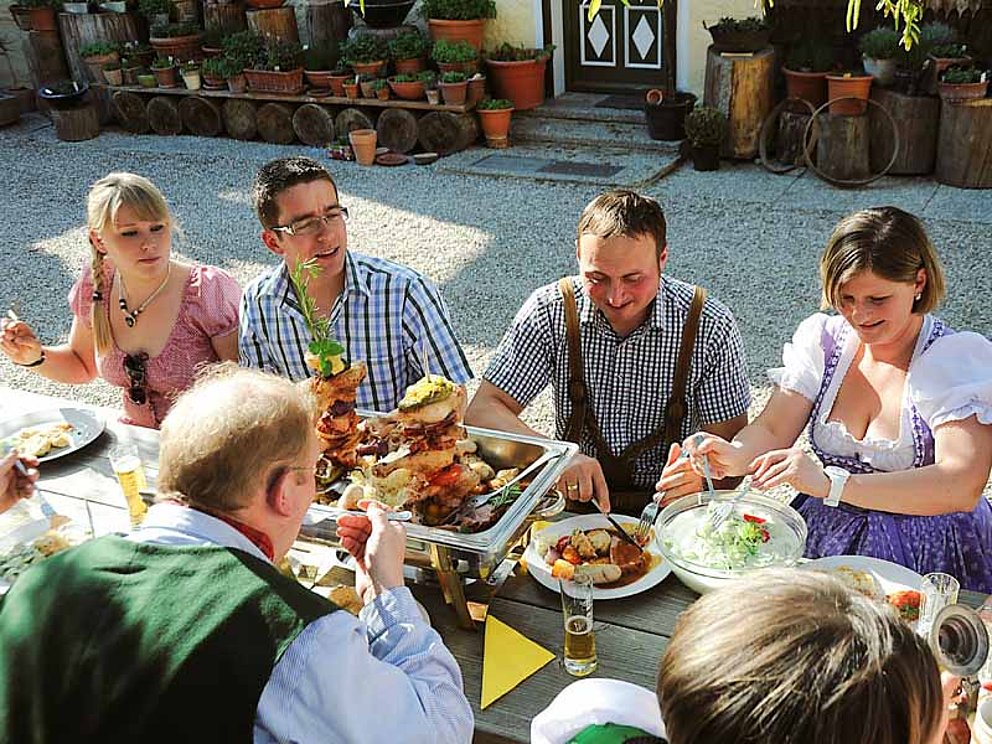 junge Leute in Tracht schmausen an einem Tisch im Innenhof am Loryhof
