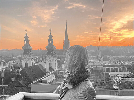 Eine Dame auf einer Aussichtsplattform über Linz in düsterem Licht.