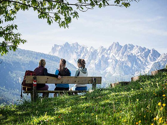 3 Damen sitzen auf einer Bank, im Hintergrund das Dachsteinmassiv