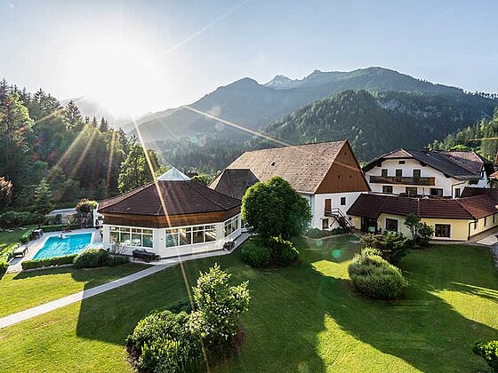 Ansicht vom Hotel Poppengut mit Garten, Pool und Nebengebäuden in ländlicher, bergiger Umgebung.