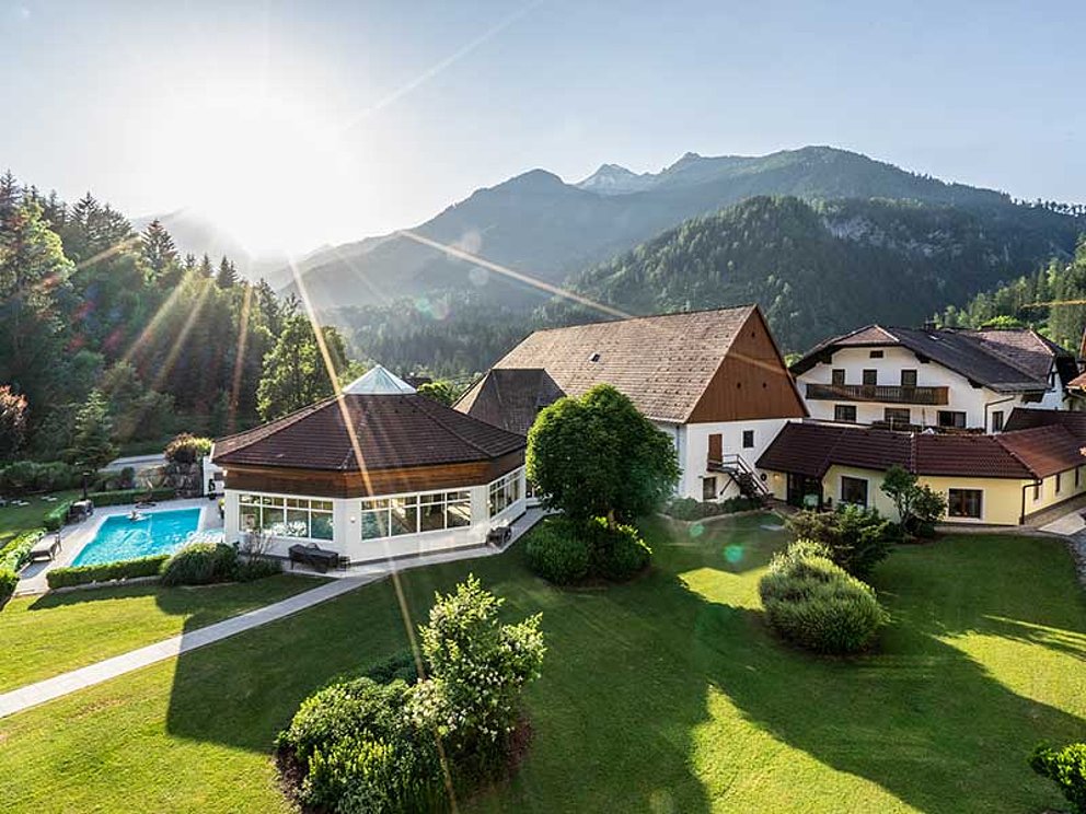 Ansicht vom Hotel Poppengut mit Garten, Pool und Nebengebäuden in ländlicher, bergiger Umgebung.
