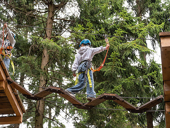 Ein Kind mit Helm und Sicherung in Action am Hochseilpark.