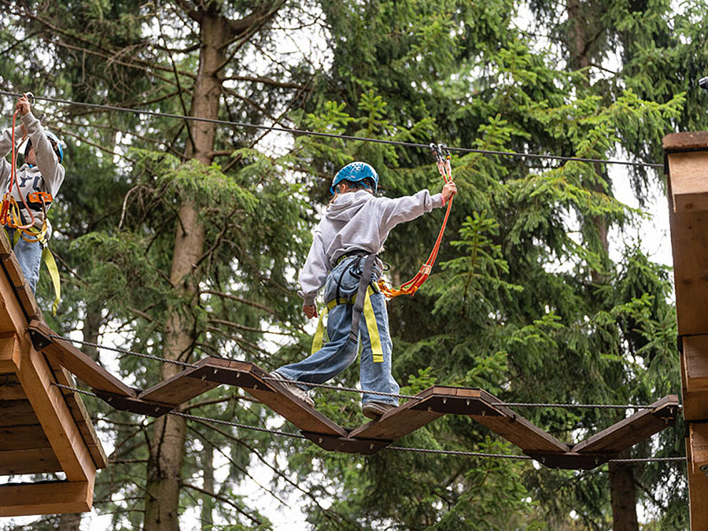 Ein Kind mit Helm und Sicherung in Action am Hochseilpark.