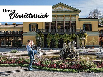 Ein Paar steht vor der Kaiservilla in Bad Ischl. Das Logo der Landesillustrierten "Unser Oberösterreich" ist als Störer im Bild platziert.