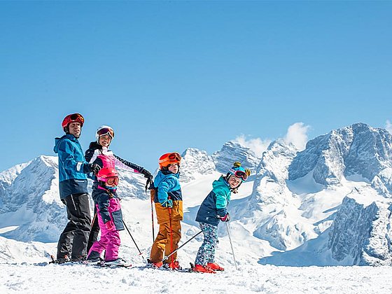 Eltern mit 2 Kindern auf Skiern vor dem Dachstein-Massiv