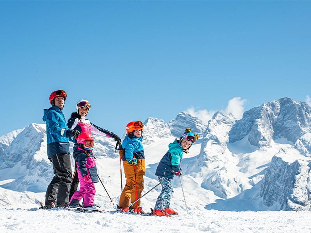 Eltern mit 2 Kindern auf Skiern vor dem Dachstein-Massiv