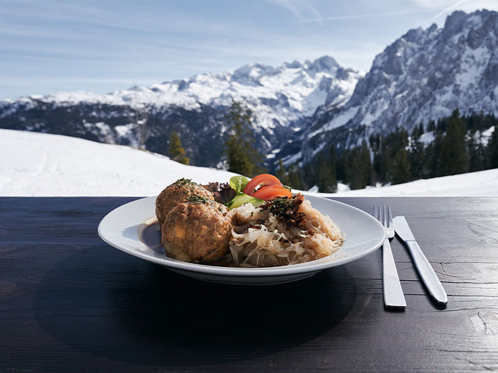 Ein Teller mit Kaspressknödel mit Kraut, im Hintergrund der Dachstein