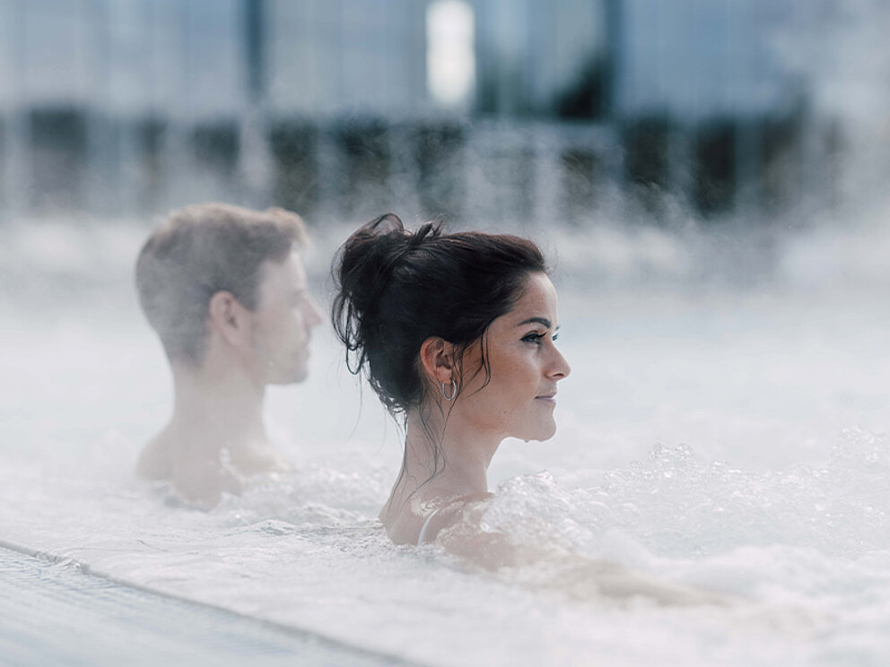ein Paar sitzt im Sprudelbad im Außenbecken der Therme