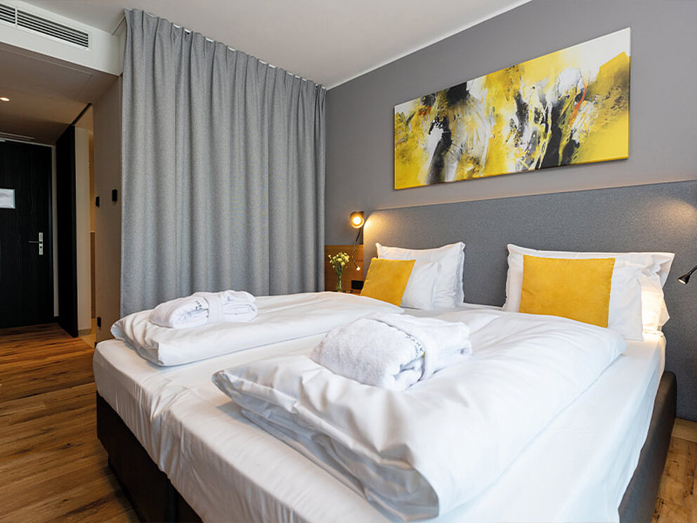 Doppelzimmer mit Holzboden, Doppelbett, Bademänteln und Vorhang vor dem offen gestalteten Badezimmern