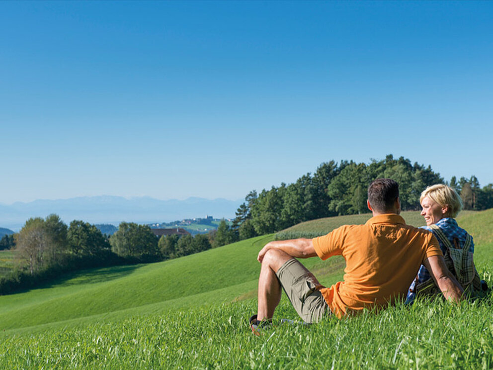 Ein Paar sitzt auf einer Wiese und schaut in die Weiten des Mühlviertels
