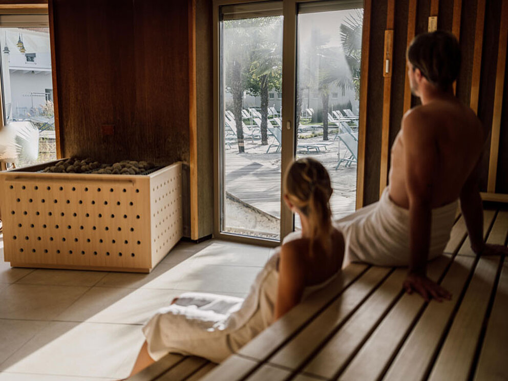 Mann und Frau sitzen in der Sauna und blicken durch das Fenster nach draußen