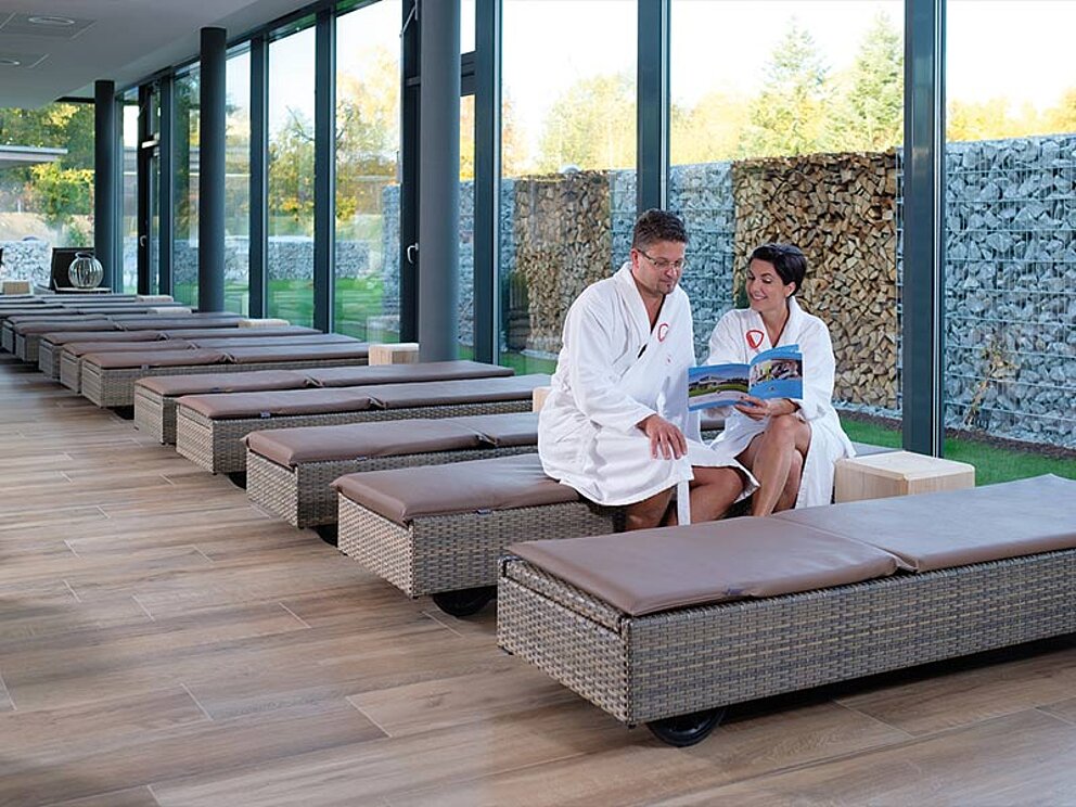 Ein Paar sitzt auf einer Liege im Ruheraum in der Therme und schmökert in einer Broschüre.