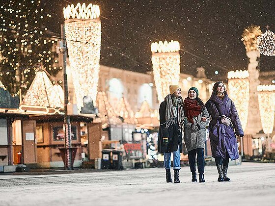 3 Damen vor dem festlich beleuchteten Weihnachtsmarkt
