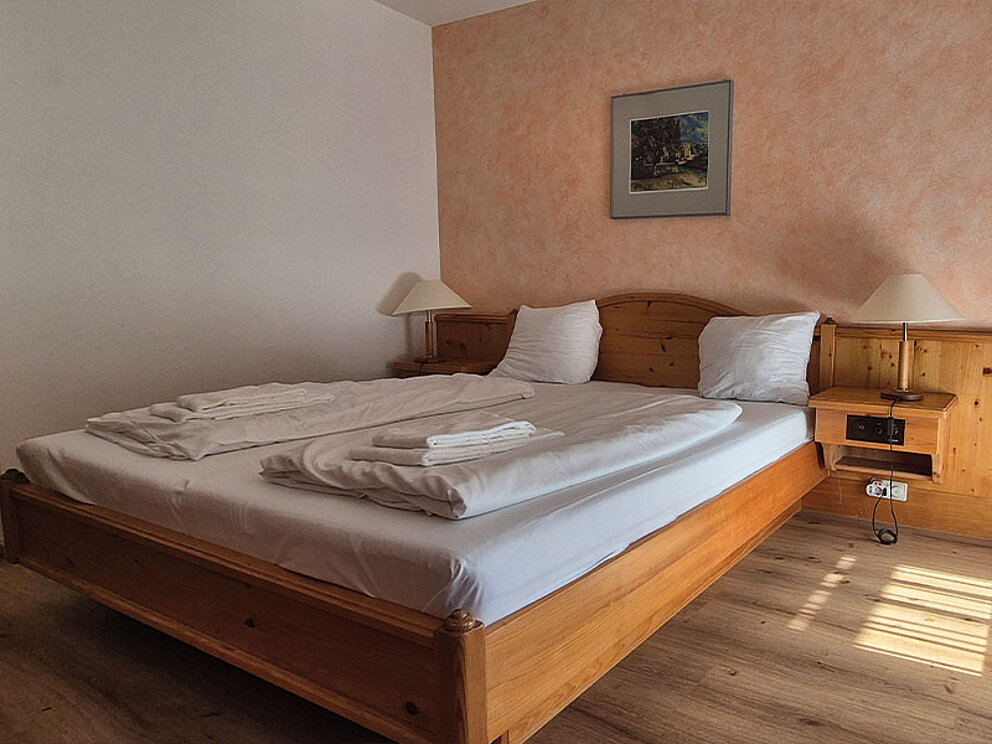 Zimmer mit Doppelbett, Nachtkästchen und Holzboden