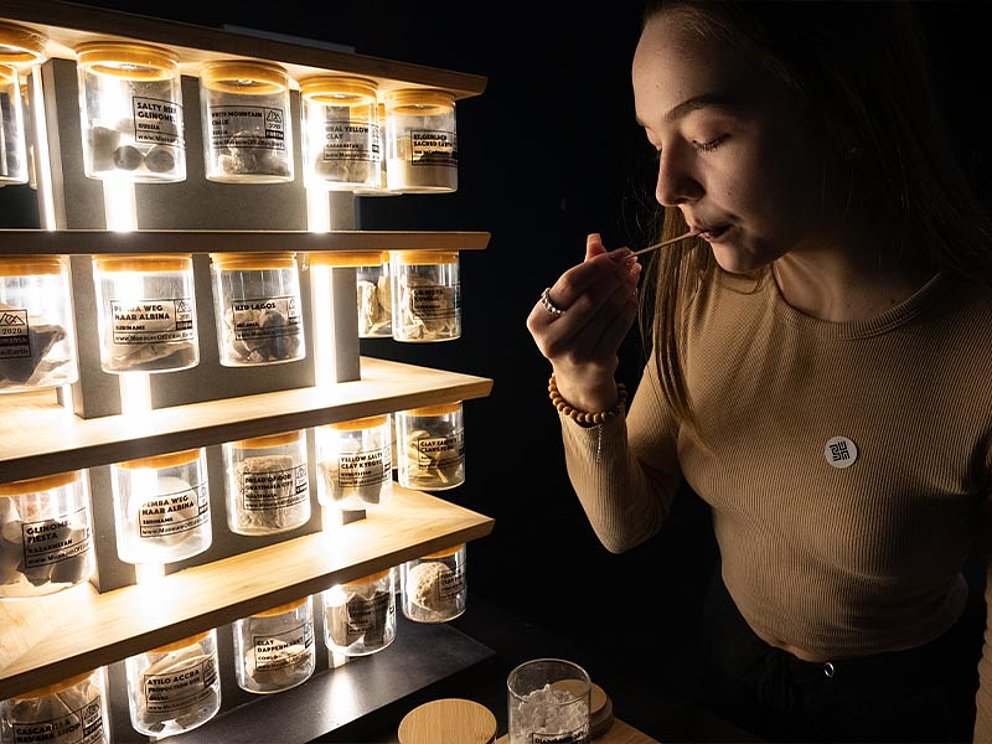 Eine Dame mit einem kleinen Holzlöffel vor vielen kleinen Glasgefäßen.