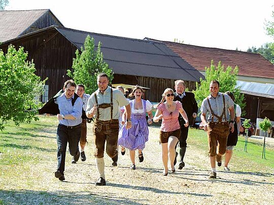 junge Leute in Tracht laufen vor einem Bauernhof