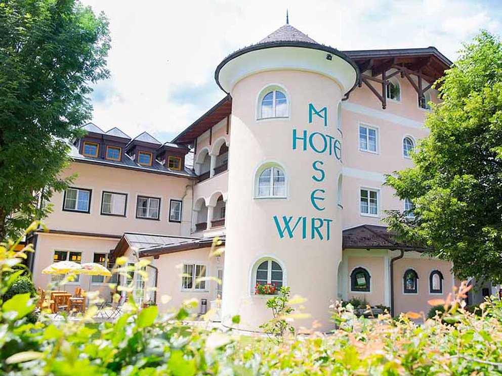 Aussenansicht Hotel Moserwirt mit Turm, umgeben von einem blühenden Garten.