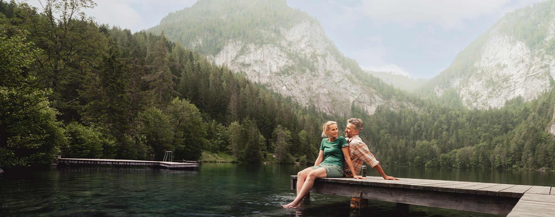 ein Paar sitzt am Steg und lässt die Füße in den See baumeln
