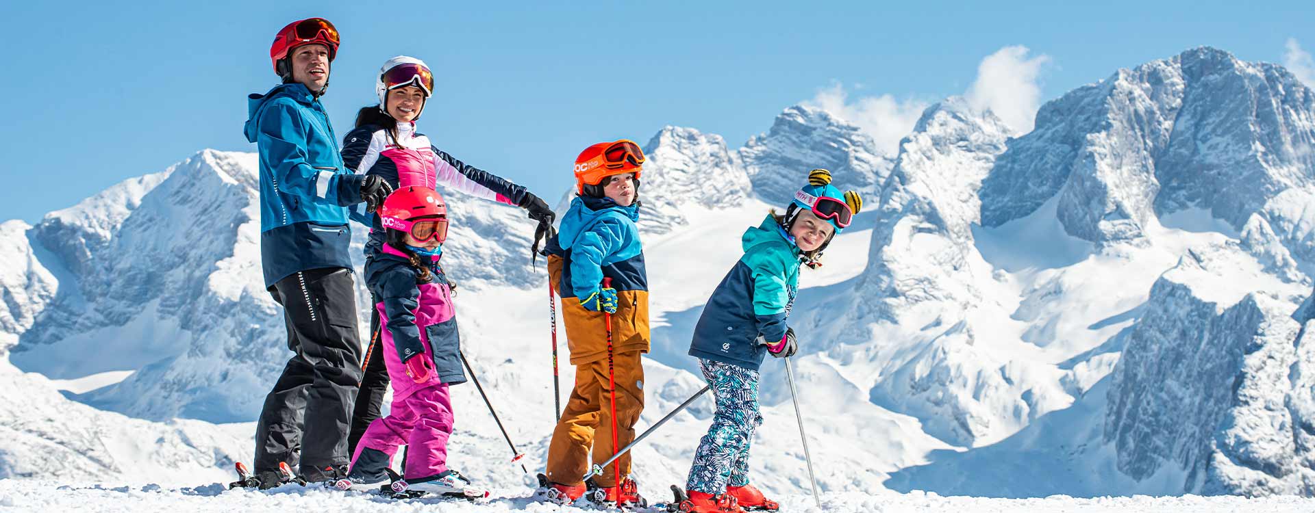 Eine Familie mit 2 Kindern auf der Piste, im Hintergrund der verschneite Dachstein